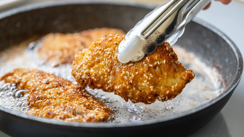 Fried chicken cutlets being removed from a hot pan with tongs