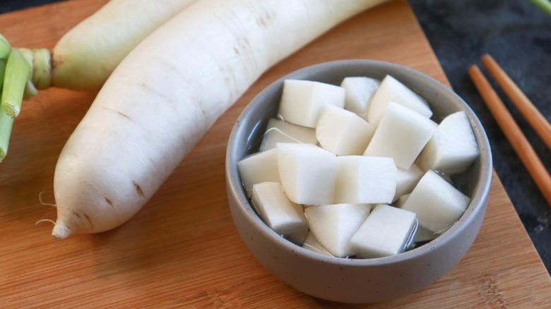 Diced pickled radish in a small bowl, next to two whole radishes.