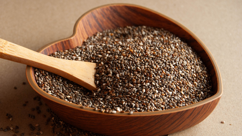 A heart-shaped wooden bowl of chia seeds with a small wooden spoon