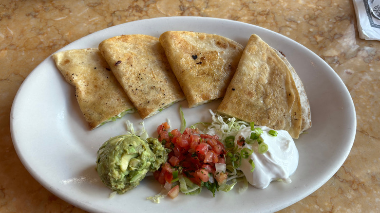 A quesadilla and side items on a white plate at The Cheesecake Factory