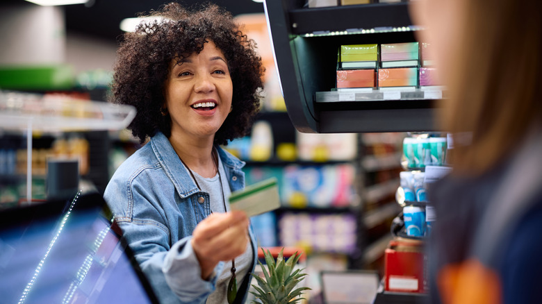 A woman handing a card to a grocery store clerk.