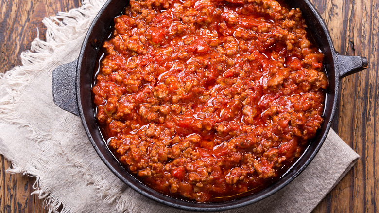 A cast iron pot of Bolognese sauce on a linen cloth over wood table backdrop
