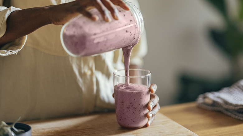 Close-up of hands pouring a smoothie into a glass.