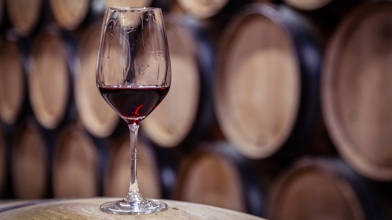 A glass of red wine in front of oak wine barrels