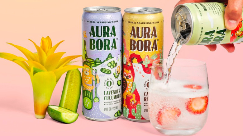 A hand pours a can of Aura Bora into a a glass next to cans with other flavors.