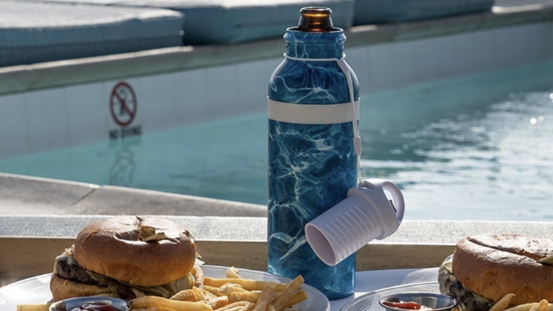 A blue BottleKeeper with a beer bottle inside served with fries and burger by the pool.