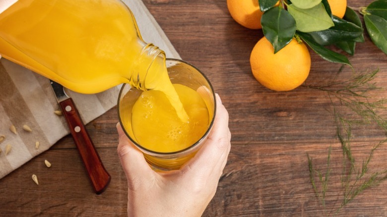 A person pouring orange juice into a glass.