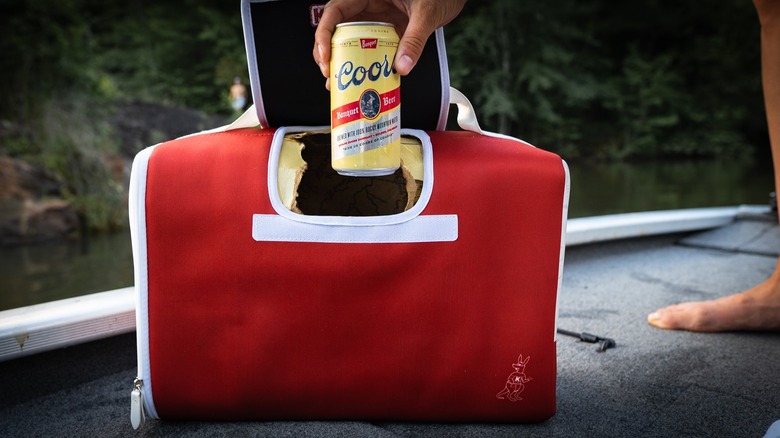 A hand lifts a beer can from a red Kanga cooler