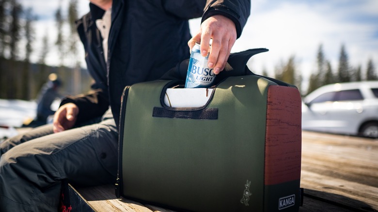 A person takes a Busch beer can from a Kanga Cooler case