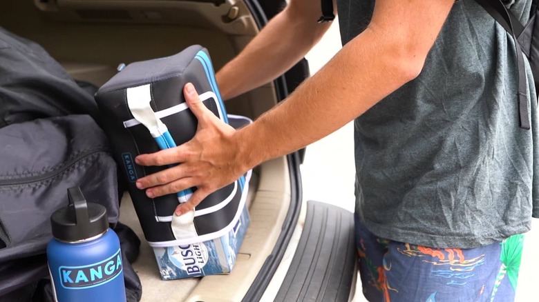 A person removes or adds a case of Busch beer to a Kase Mate in a car trunk