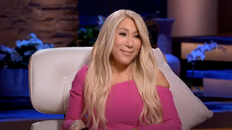 Lori Greiner, dressed in pink, smiles while listening to a presentation on "Shark Tank."