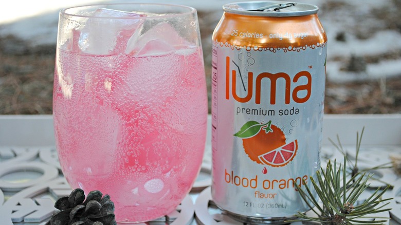 A can of Luma soda, Blood Orange flavor next to a glass with the beverage inside and some ice