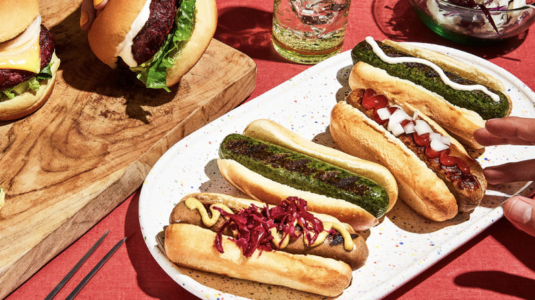 Hot dog sandwiches, burgers, and a salad served on a red table, along with drinks.