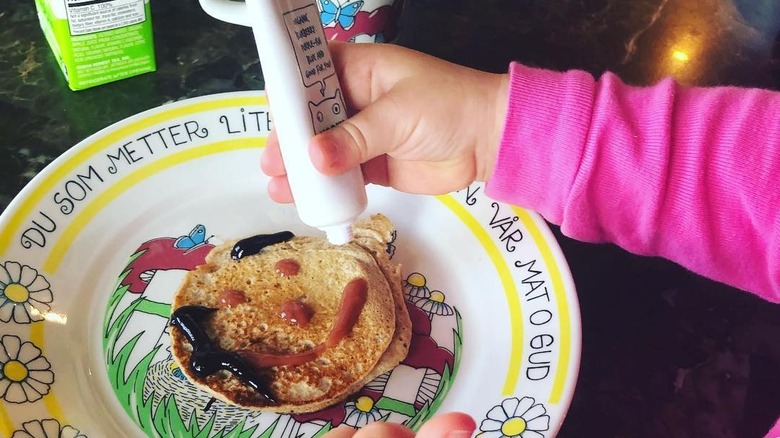 A kid painting a smiley face on a pancake using Noshi