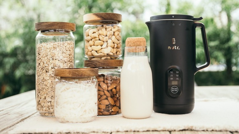 A black Nutr machine surrounded by containers filled with almonds, cashews, oats, milk, and more
