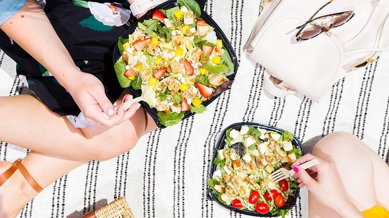 Two people on a blanket holding boxes of Wendy's salads