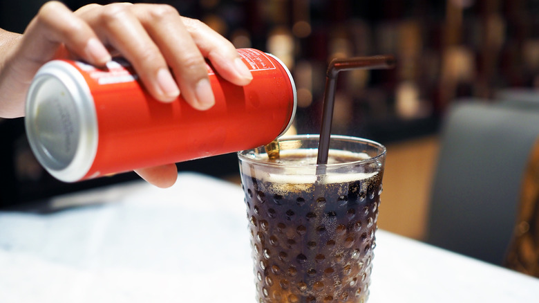 A closeup of a hand pouring a coke into a glass with a straw