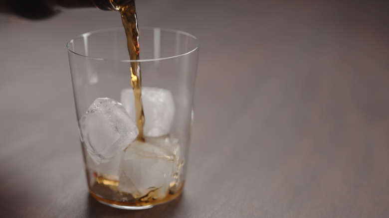 A closeup of a glass of ice with a brown liquid being poured over it