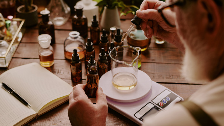 A man mixes essential oils using a small scale on a wooden table