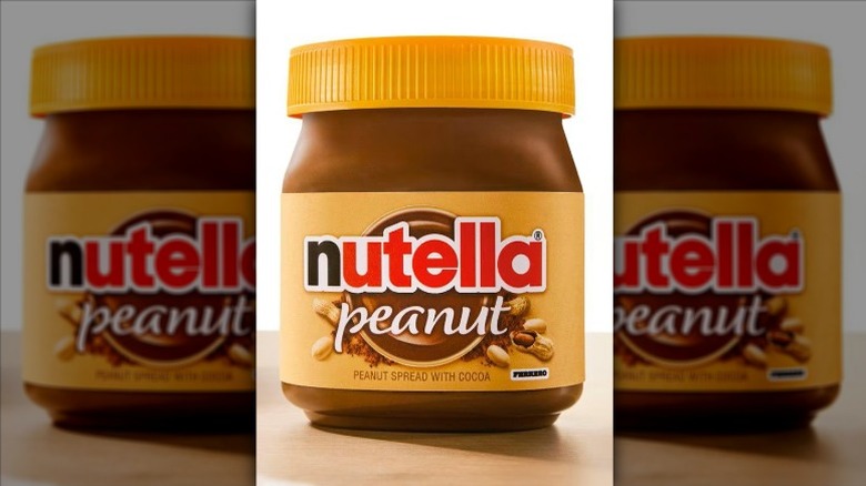 A jar of Nutella Peanut Spread sitting on a wood surface with a white background.