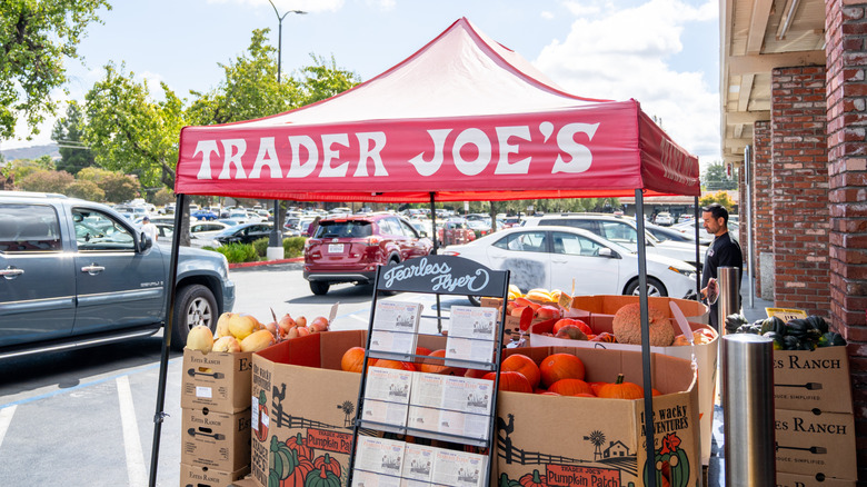 A Trader Joe's pumpkin stand outside of a busy Trader Joe's location during the day.