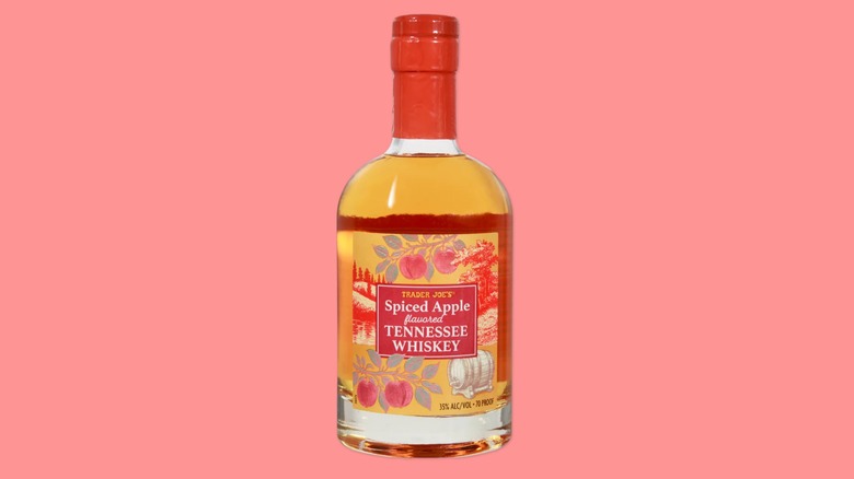 A bottle of the Spiced Apple Flavored Tennessee Whiskey from Trader Joe's on a pink background.