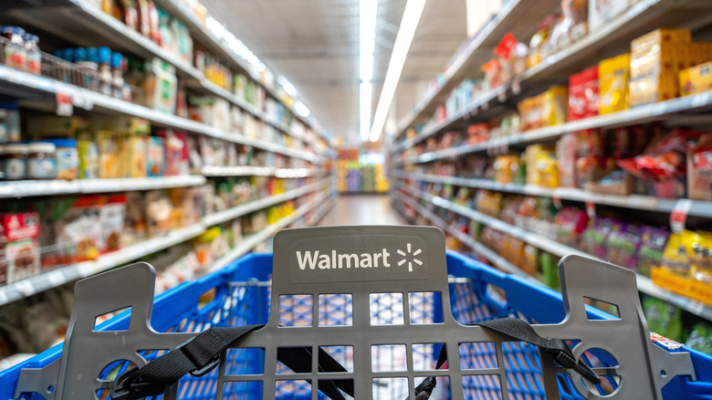 A Walmart shopping cart in the middle of a grocery aisle of a Walmart store.