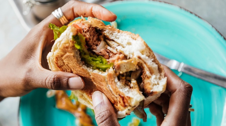Two hands holding a vegan burger with bites taken out of it