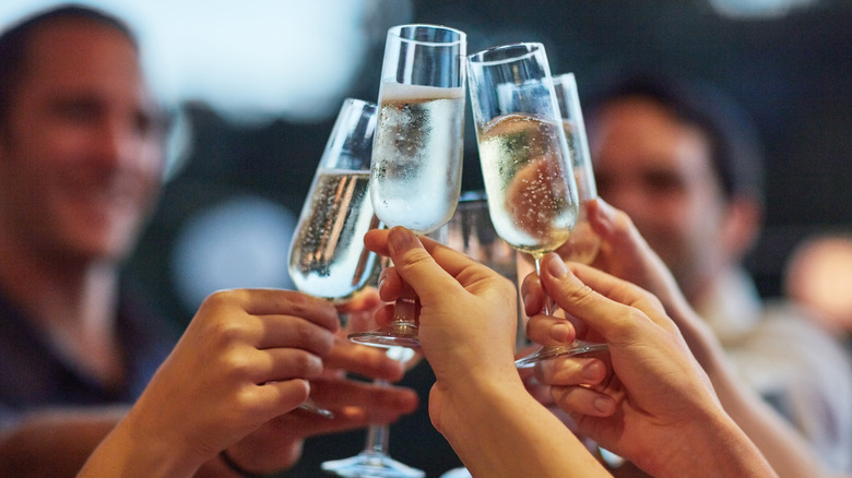 Hand pours sparkling wine into four wine glasses