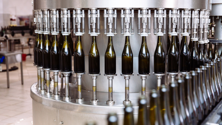 A machine bottles wine in dark green bottles