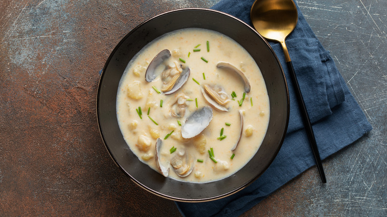 Black bowl of clam chowder with gold spoon and blue napkin