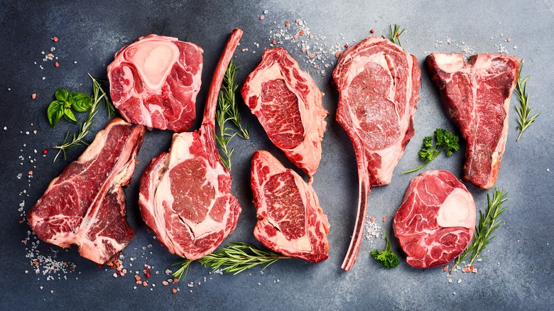 a top-down view of several different cuts of raw steak with good marbling on them.