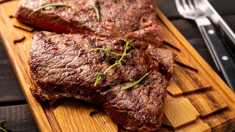 A slab of steak cut in two on a wooden board.