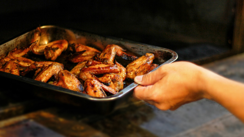 hand taking a pan of chicken wings out of the oven