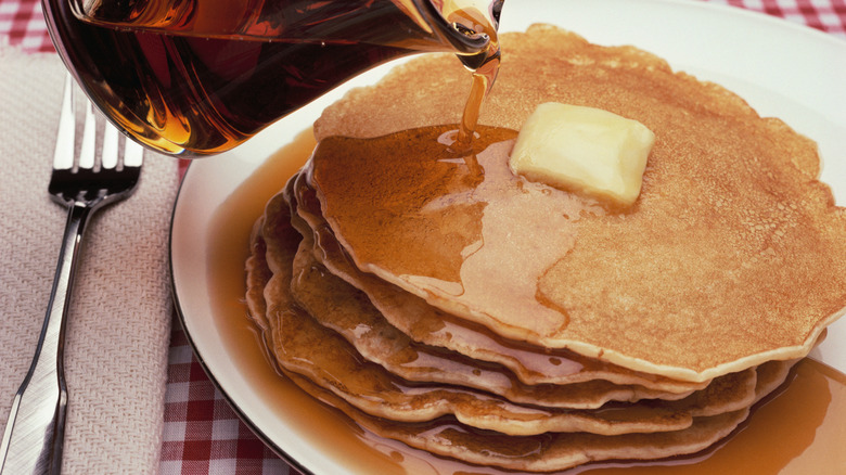 Pouring syrup on a stack of pancakes with a pat of butter