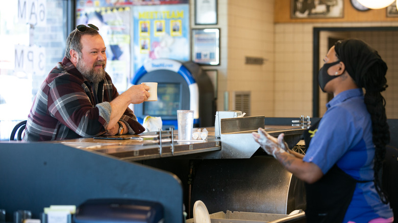 A man sitting alone at the front counter of Waffle House speaking to a cook and drinking coffee