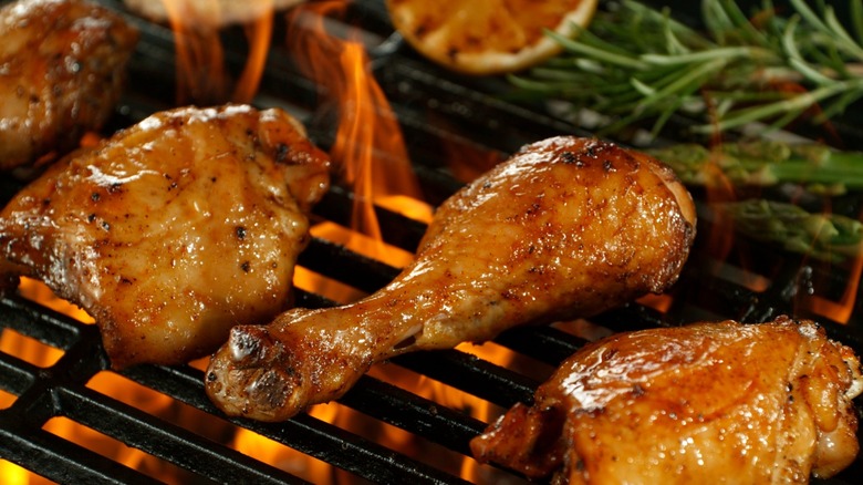 Chicken and hearty herbs cook on a grill over flames