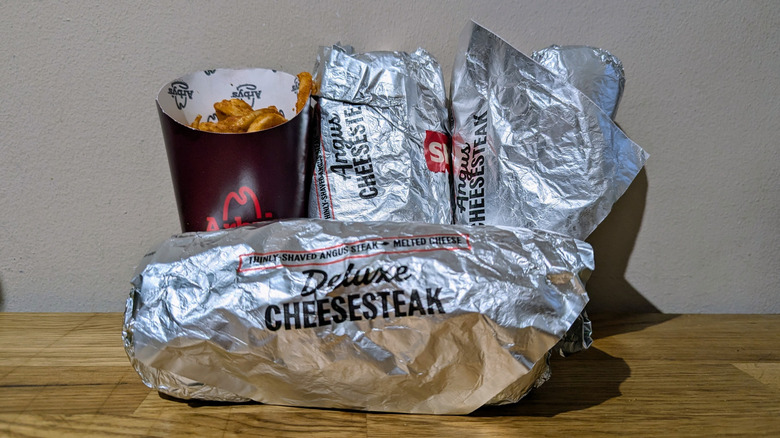 Arby's three new Chicken Cheesesteaks in foil wrappers with curly fries.