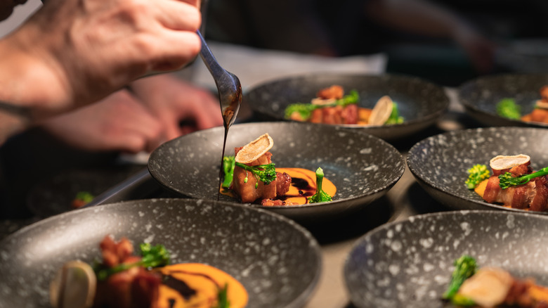 hand drizzling sauce over a fancy dish next to other plated dishes