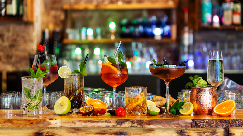 Assortment of cocktails on a wooden bar with a bar setting blurred in the background.