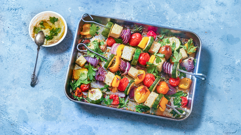 A sheet pan topped with tofu kebabs, sauce on side