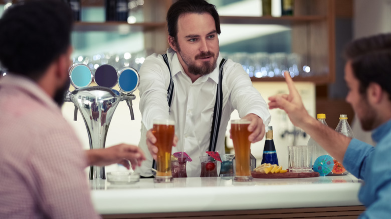 Two guys speaking to a bartender as he gives them their glasses of beer.