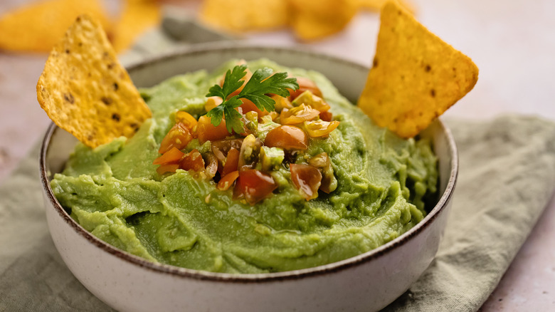 a bowl of guacamole with chips and tomatos