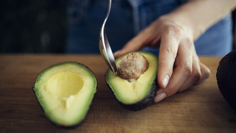 hands prepare perfectly ripe cut avocado with spoon