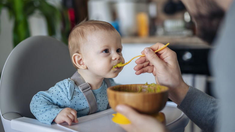 A father feeds his child food from a bowl.