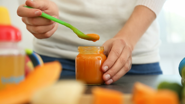 A woman preparing homemade baby food in a glass jar.