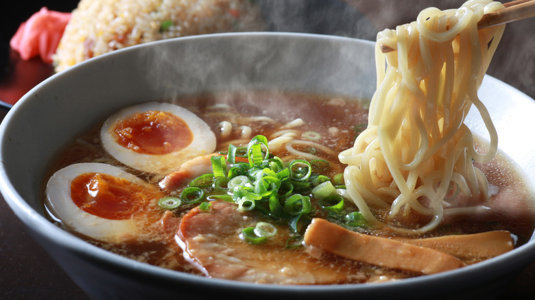 Using chopsticks to gather noodles from a bowl of ramen with eggs and meat