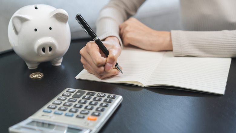 A woman holding a pen and budgeting with a piggy bank nearby