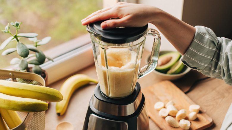 woman places hand on top of blender with smoothie