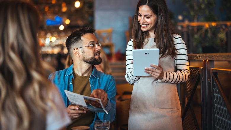 A customer orders food from a server while pointing at a menu